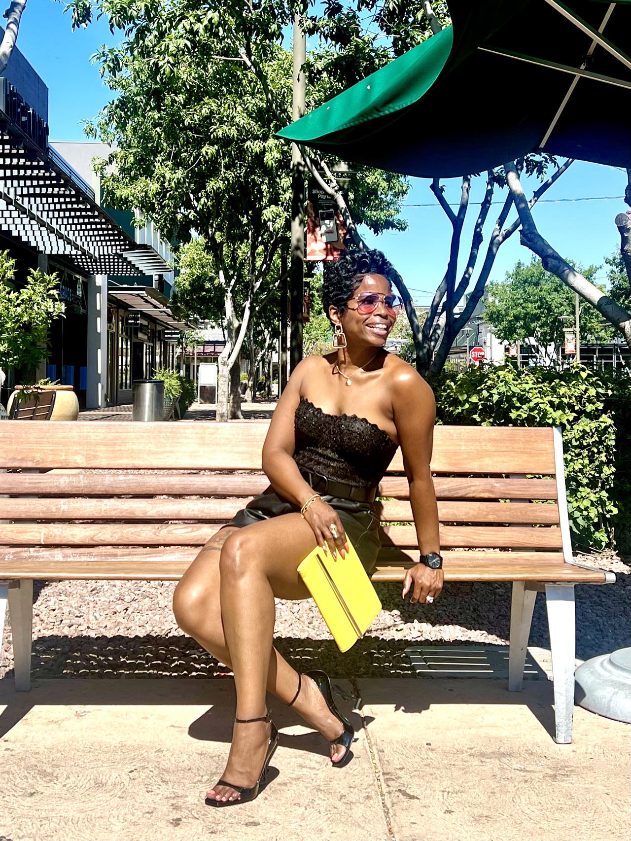 Black bustier black leather shorts yellow purse sitting on bench