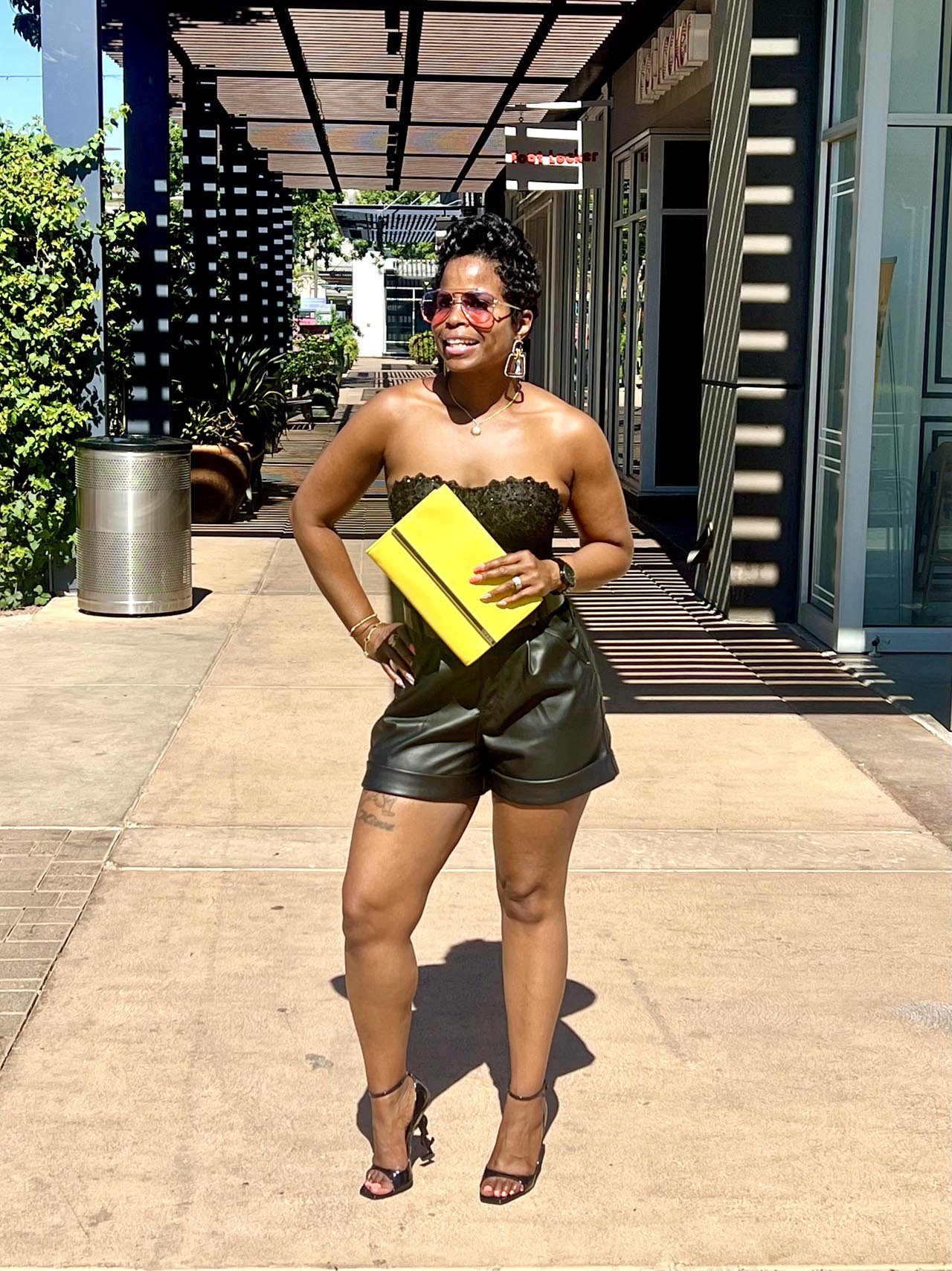 Black bustier black leather shorts with yellow purse hand hand on hip